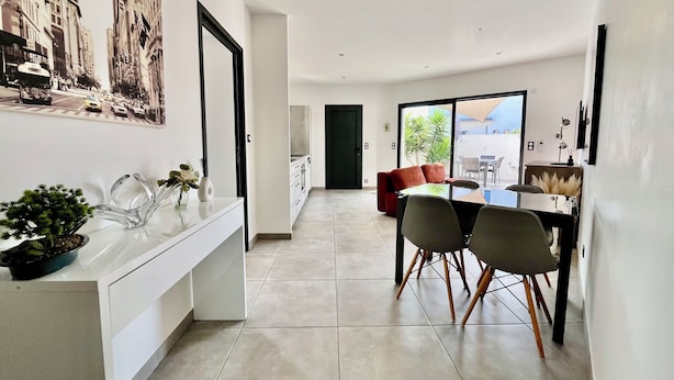 Una cocina moderna con encimera blanca, zona de comedor con mesa y sillas, y un sofá rojo al fondo.