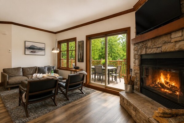 A cozy living room with a stone fireplace, a sofa, a coffee table, and a dining area with chairs.
