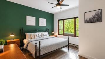 A bedroom with a bed, nightstands, a ceiling fan, a window with a view, and framed inspirational quotes.