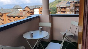 En balkon med bord og stole, udsigt over et bjergrigt område med træhuse.