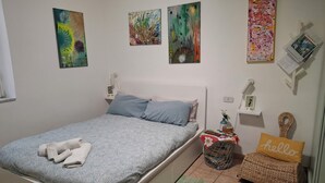 Ein ordentlich eingerichtetes Schlafzimmer mit einem Bett, Kissen, einem kleinen Tisch, einem Korb und Wandbildern.