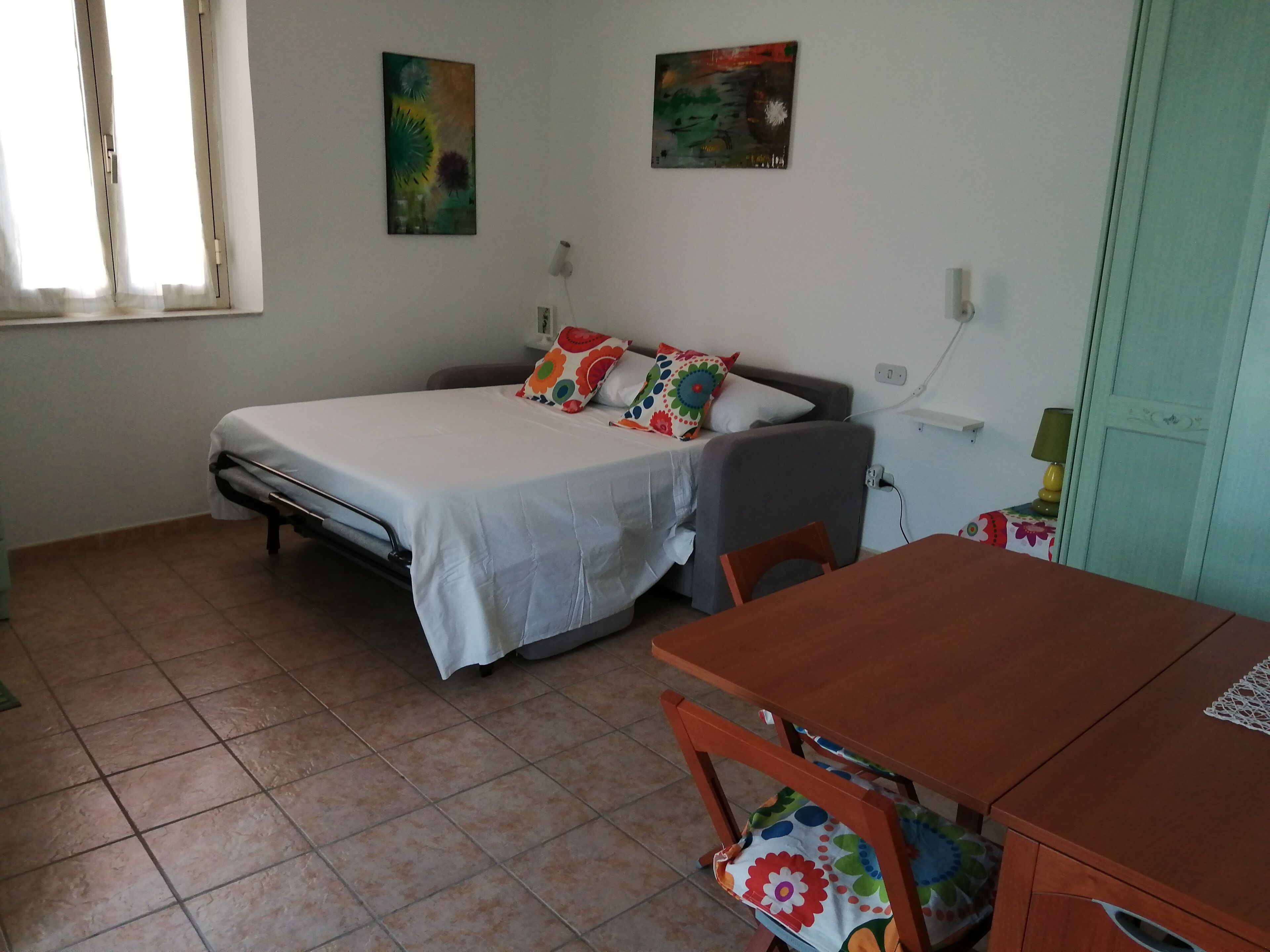 Een slaapkamer met een bed, een klein tafeltje en twee schilderijen aan de muur.