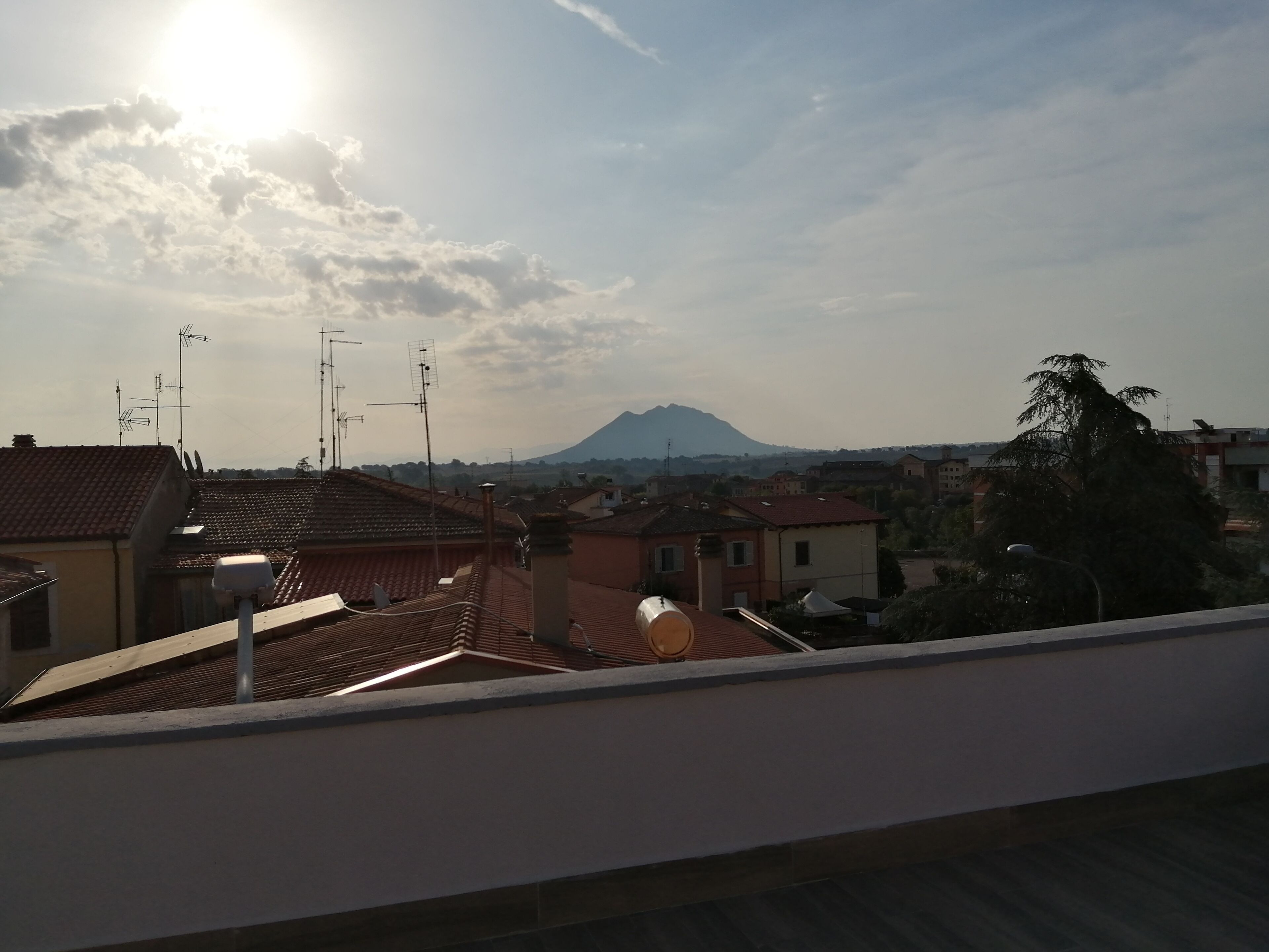 Un tetto con parabole, una montagna sullo sfondo e cielo sereno.