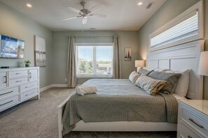 Een slaapkamer met een bed, een kaptafel, een plafondventilator en een raam met gordijnen.