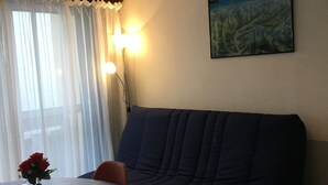 A cozy living area with a sofa, a dining table with chairs, a vase with flowers, and a painting on the wall.