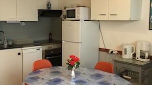 A compact kitchen with white cabinets, a microwave, a refrigerator, and a dining table with orange chairs.