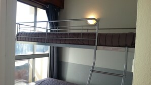 A bunk bed with a window and curtains, a bedside table, and a wall-mounted light.