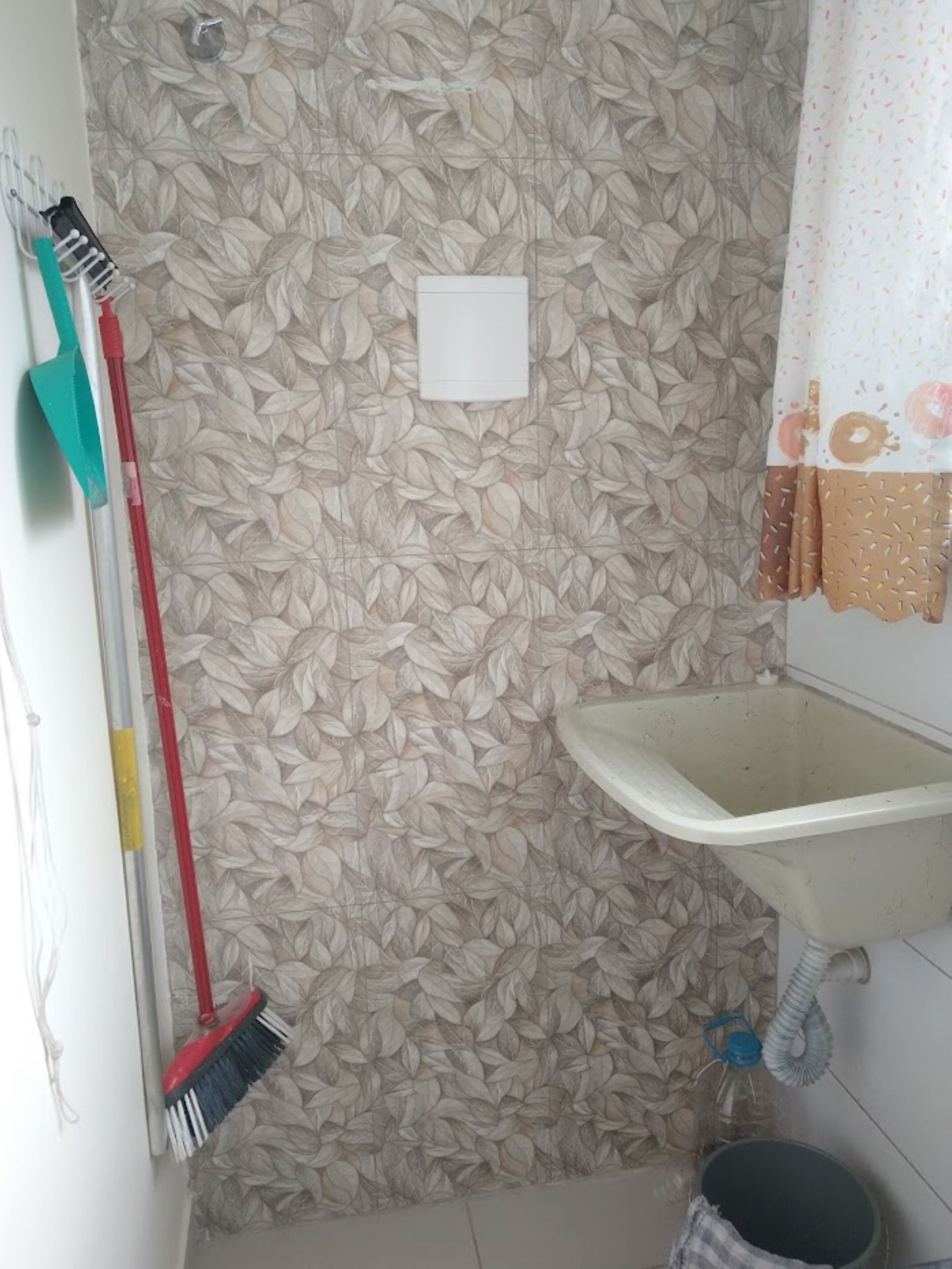 Une salle de bain avec un mur orné d’un motif de feuilles, un lavabo blanc et un espace douche.