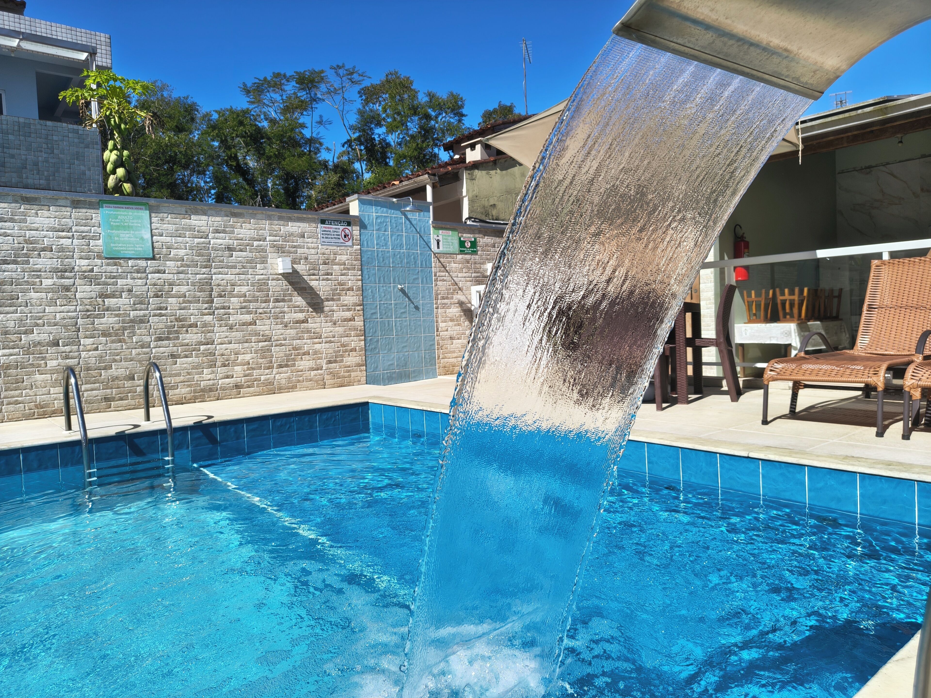A swimming pool with a water feature, a stone wall, and a lounge area with chairs.