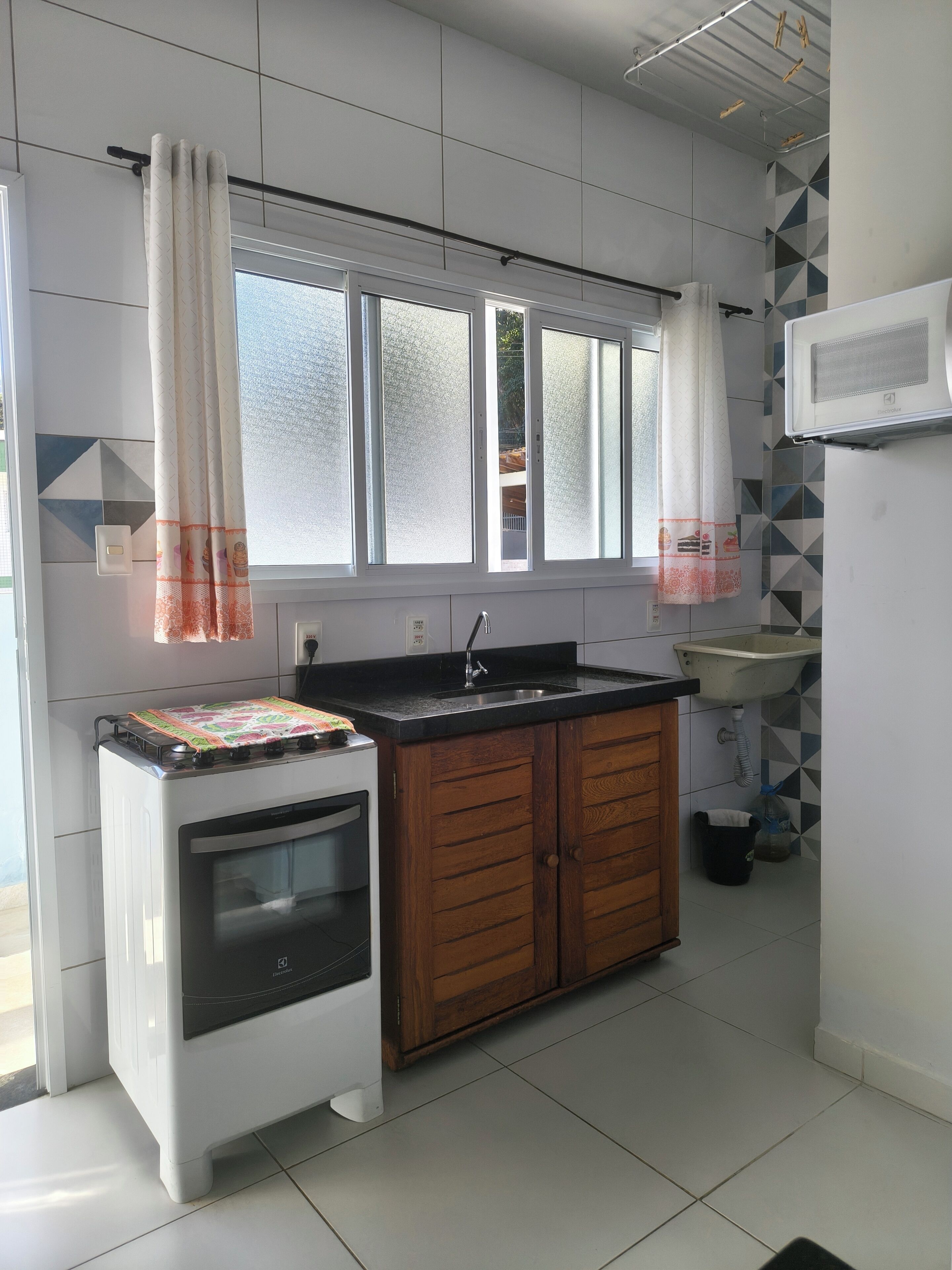 A kitchen with a stove, oven, wooden cabinets, a sink, and a window with curtains.