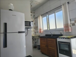A compact kitchen with a refrigerator, microwave, sink, and oven. - Canto Verde Aptos II (Caraguatatuba)