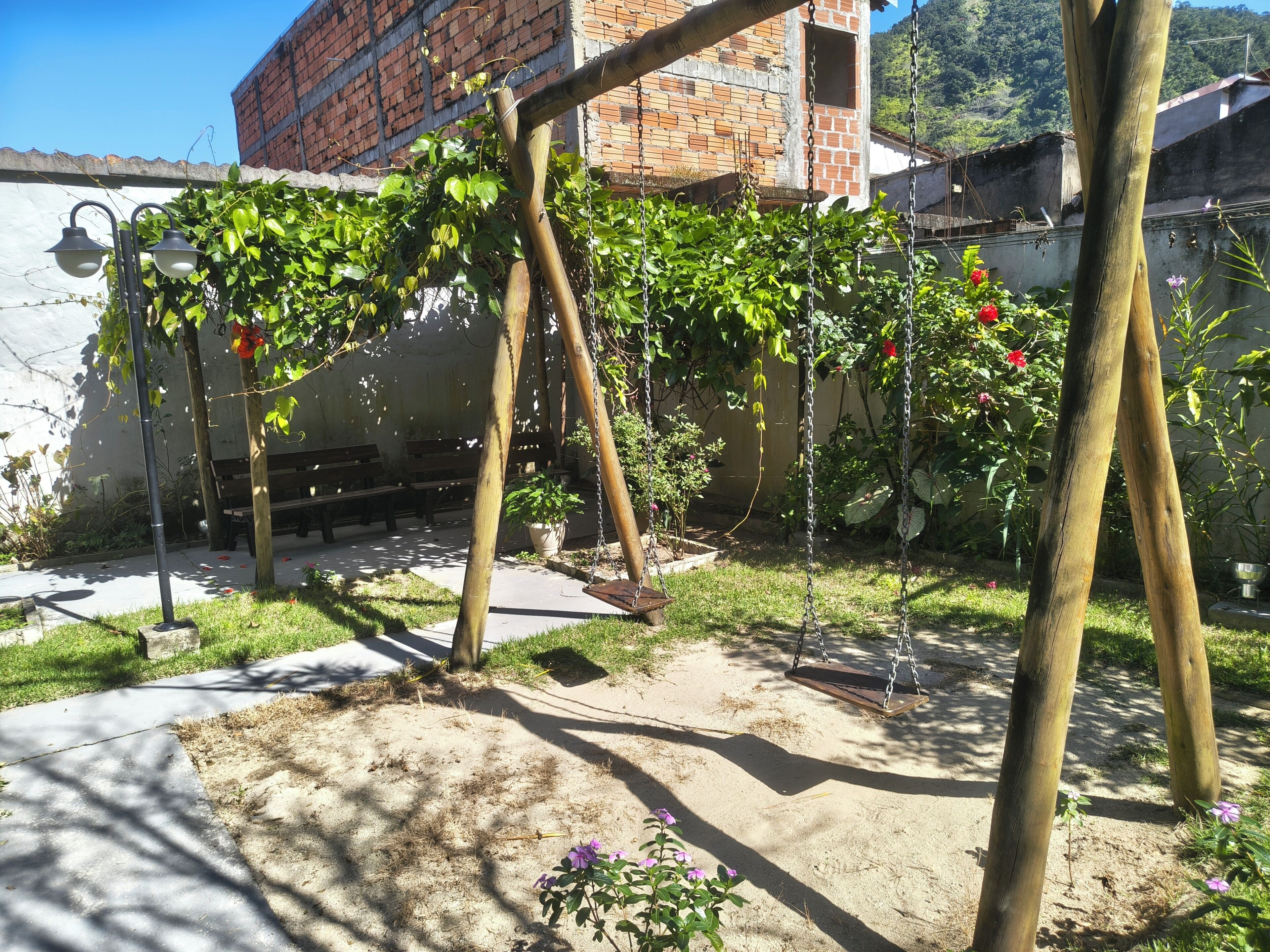 A garden with a swing set, a brick building, and a bench area.