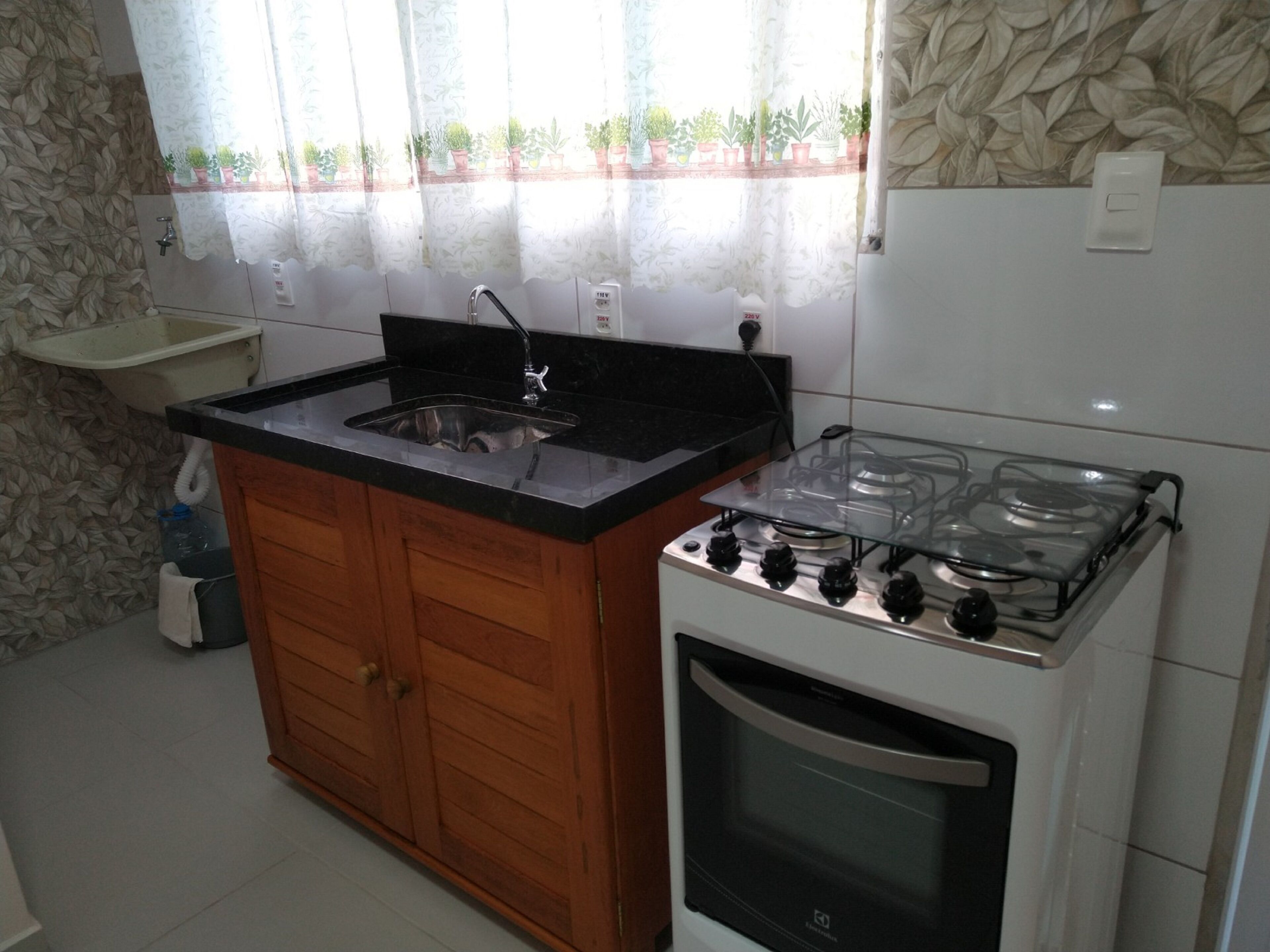 Una cocina con un armario de madera, un fregadero, una estufa y una ventana con cortinas.