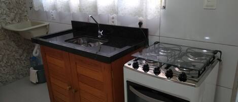 Una cocina con un armario de madera, un fregadero, una estufa y una ventana con cortinas.
