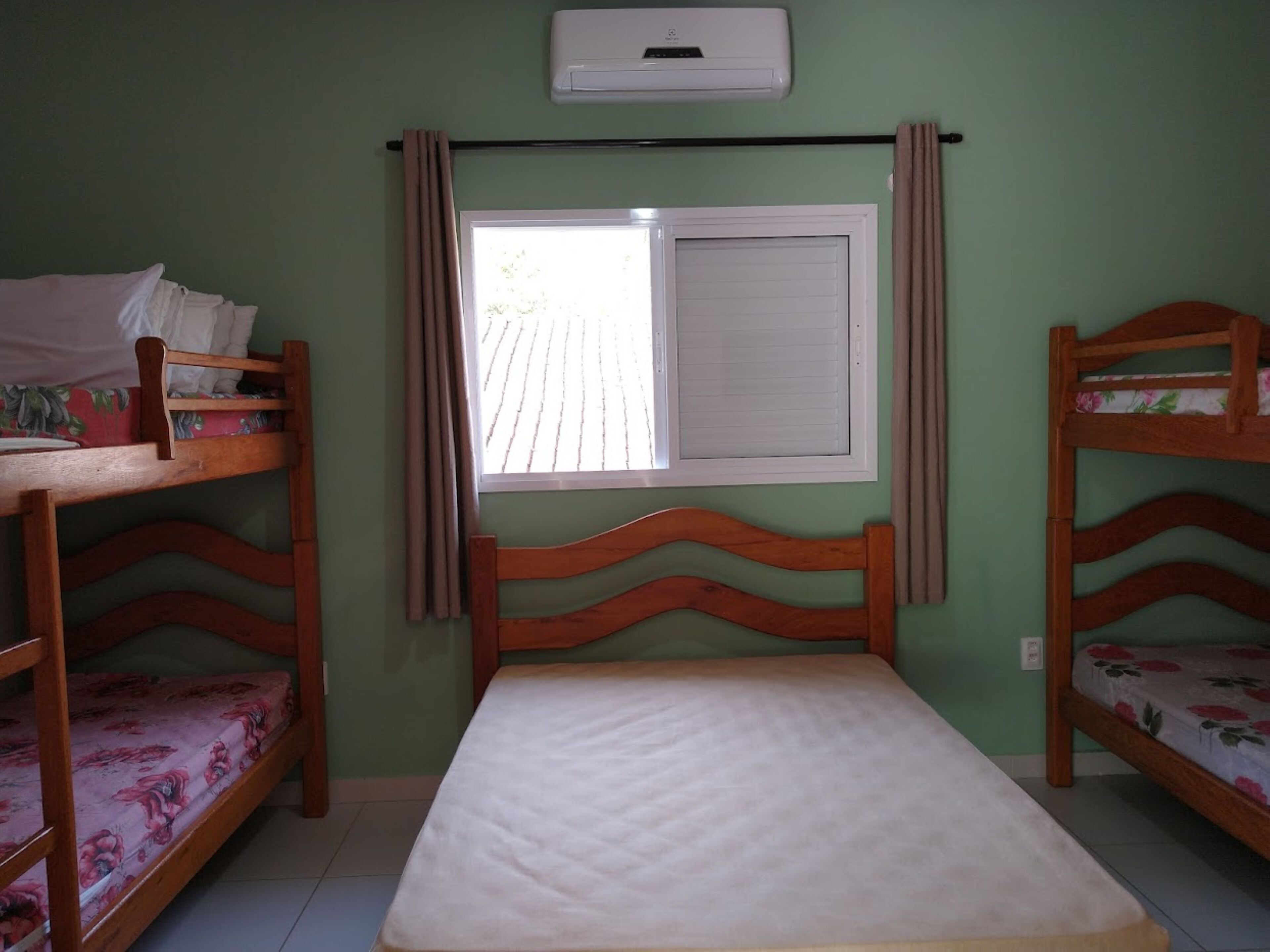 Um quarto de dormitório com beliches, uma janela com cortinas e um aparelho de ar condicionado.