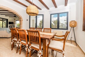 A dining area with a wooden table and chairs, a woven light fixture, and large windows with a view. - 3 Bedroom Villa in Quiet Area (Javea / Xàbia)