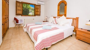 A bedroom with a large bed, a wooden wardrobe, a chair, and a window with open shutters.