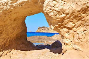 A natural rock formation with a cave-like opening leading to a beach and the sea.