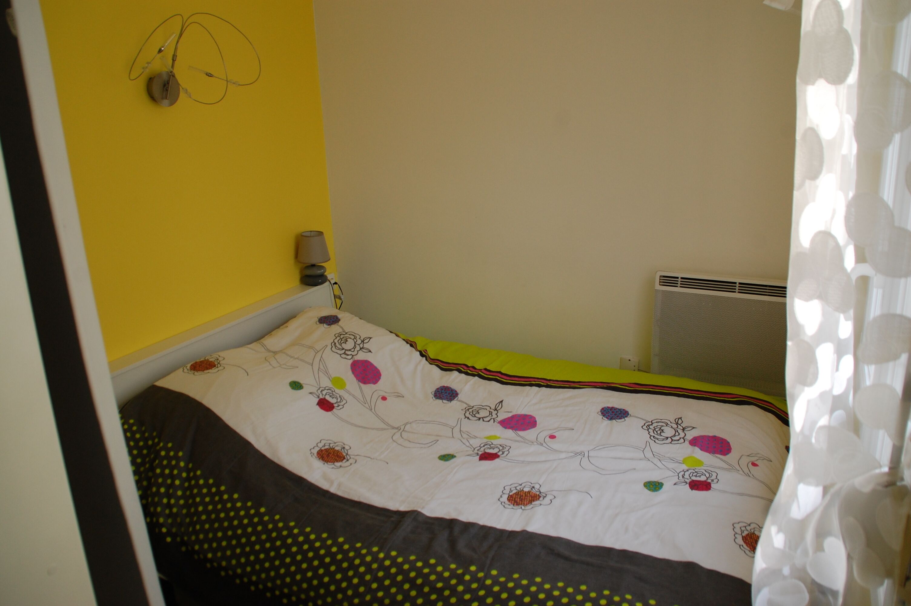 A bedroom with a bed, a wall-mounted lamp, and a radiator.