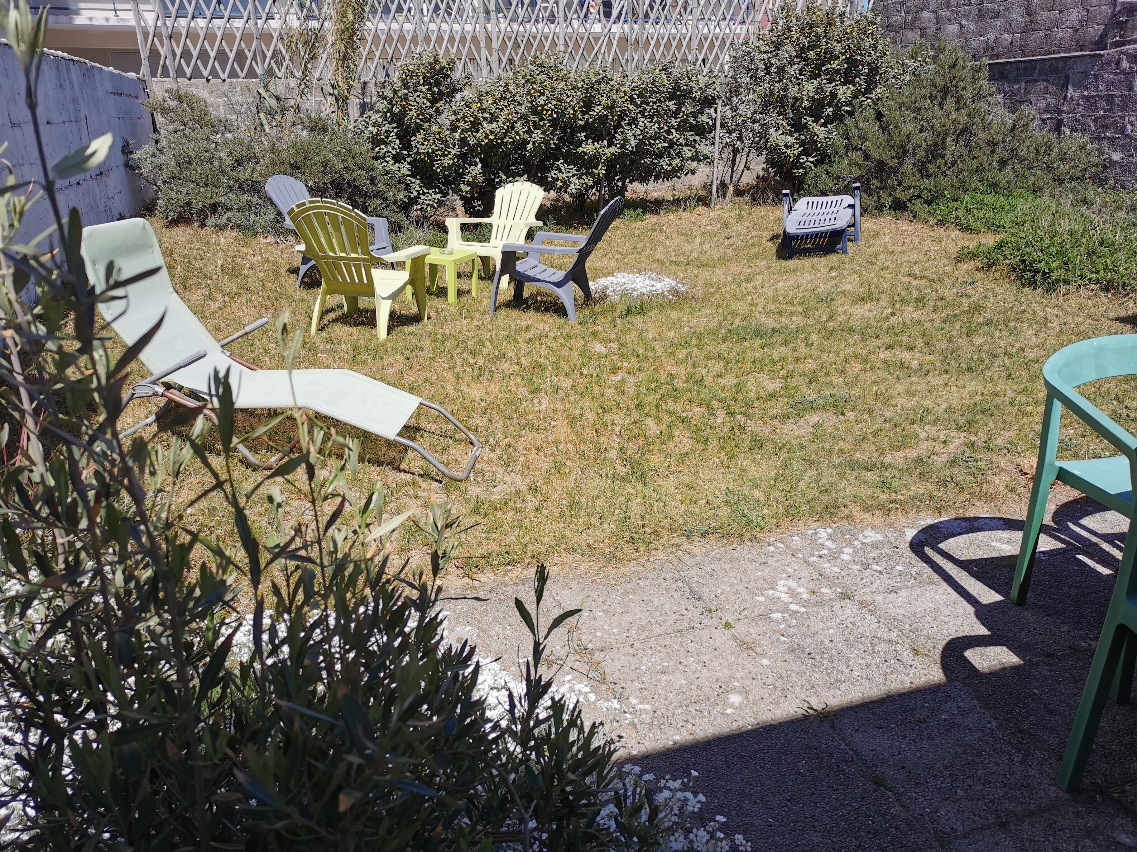Eine Terrasse mit Gartenmöbeln, darunter Stühle und ein Tisch, umgeben von Gras und Pflanzen.