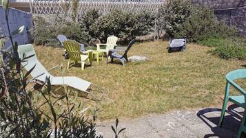 Eine Terrasse mit Gartenmöbeln, darunter Stühle und ein Tisch, umgeben von Gras und Pflanzen.