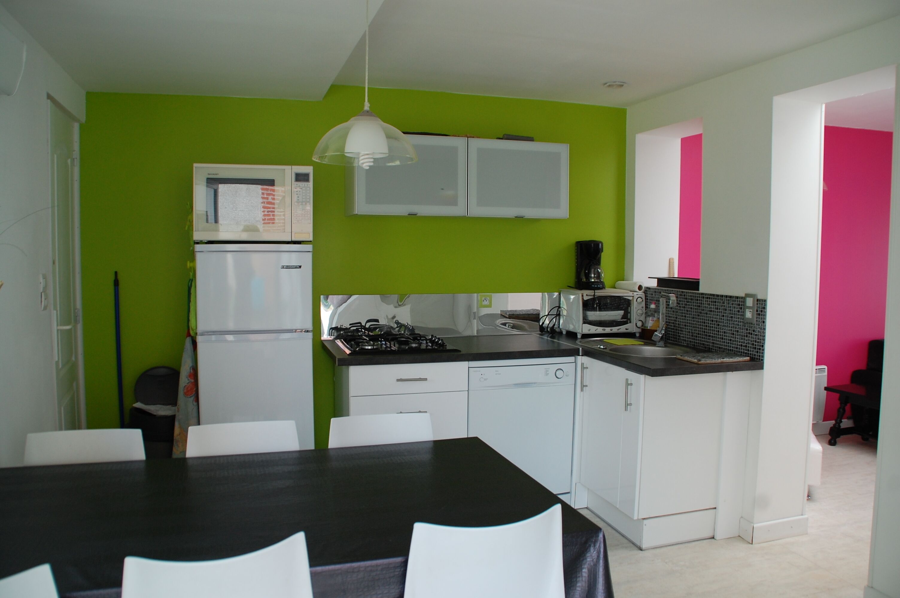 Een kleine keuken met witte kastjes, een zwart aanrecht en een groene wand.