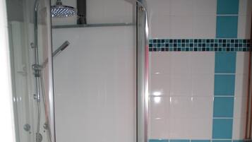 A bathroom with a glass-enclosed shower, a toilet, and a blue bath mat.
