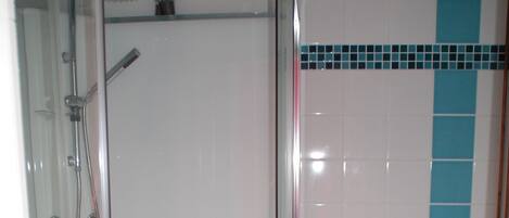 Un baño con ducha de vidrio, inodoro y alfombrilla de baño azul.