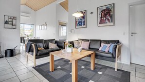 Un salon moderne avec un plafond en bois, deux canapés en cuir noir, une table basse en bois et un tapis à motifs.