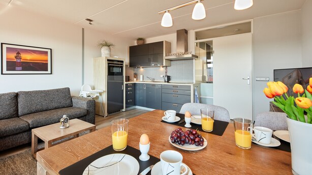 Una sala moderna con sofá, mesa de comedor y cocina al fondo.