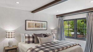 Un dormitorio con una cama, una mesita de noche, una lámpara, una ventana con cortinas y un cuadro en la pared.