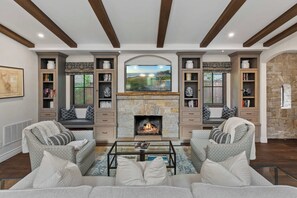 A spacious living room with a stone fireplace, built-in bookshelves, and a large flat-screen TV mounted above the fireplace.
