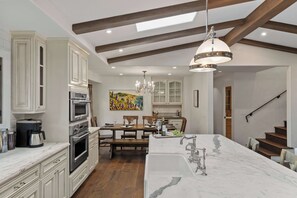 Una cocina moderna con armarios blancos, una isla de mármol y un comedor con mesa y sillas de madera.