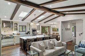 Una cocina amplia con electrodomésticos modernos, un comedor con una isla grande y una sala de estar acogedora con sofá y una mesa de centro de vidrio.