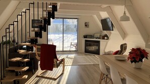 Ein modernes Loft mit schrägedem Dach, einer Treppe mit schwarzen Geländern, einem Kamin und einem Essbereich mit Tisch und Stühlen.