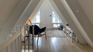 Ein Dachzimmer mit hohen Decken, Holzboden, einer weißen Tür und Blick durch ein großes Fenster nach draußen.