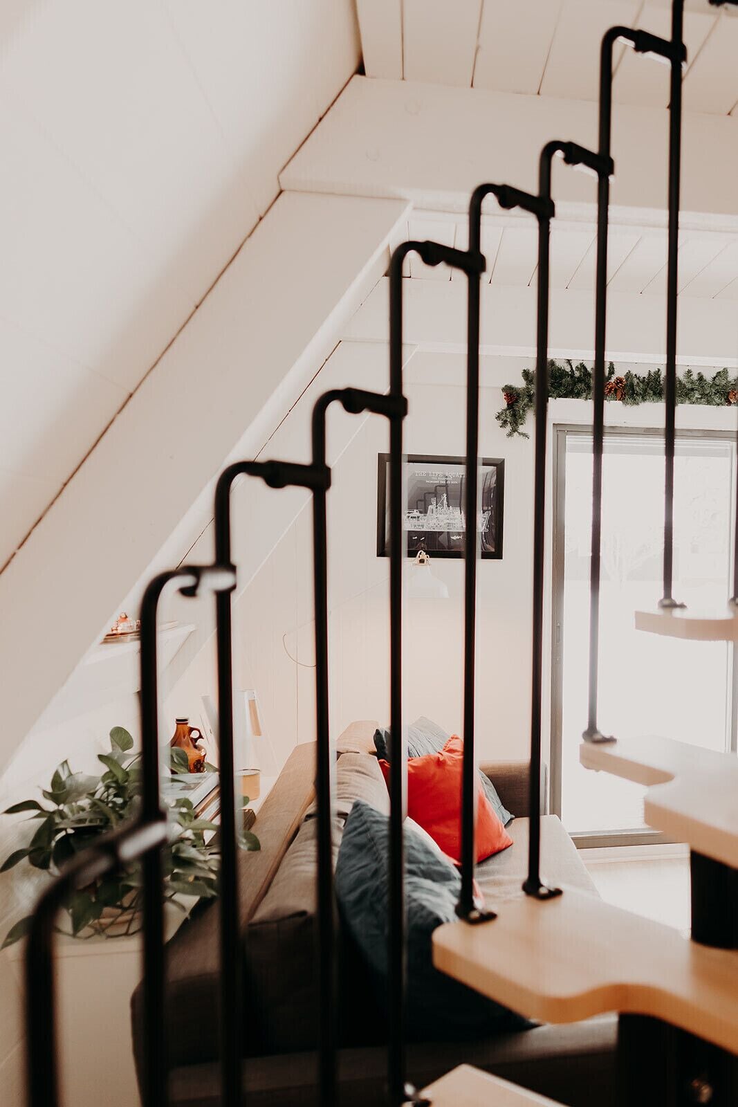 A staircase with a black metal railing, a sofa with cushions, and a small table with a plant.