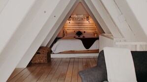 Ein gemütliches Schlafzimmer im Dachgeschoss mit schrägen Wänden, einem Bett mit Holz Kopfteil und einem Sessel.
