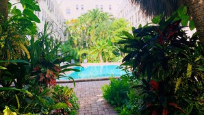 Zona de piscina rodeada de exuberante vegetación tropical y un edificio con múltiples ventanas al fondo.