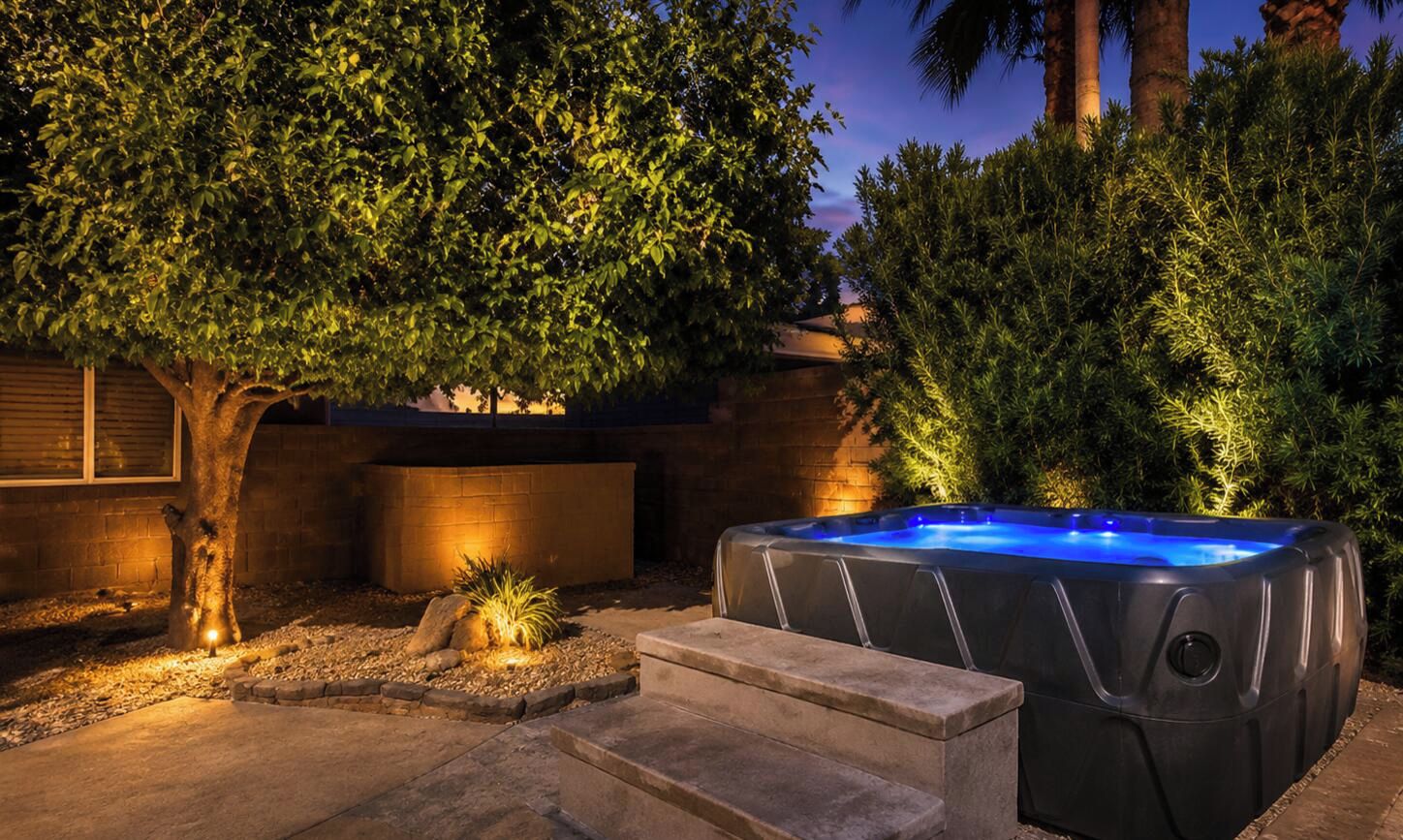 A hot tub in a landscaped outdoor area with steps leading up to it, surrounded by trees and a brick wall.