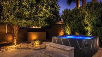 A hot tub in a landscaped outdoor area with steps leading up to it, surrounded by trees and a brick wall.