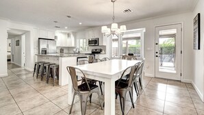 Una cocina amplia con una isla central, muebles blancos y un comedor con una mesa y sillas blancas.