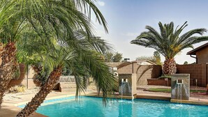 Una piscina con palmeras, un muro de ladrillo y una fuente.