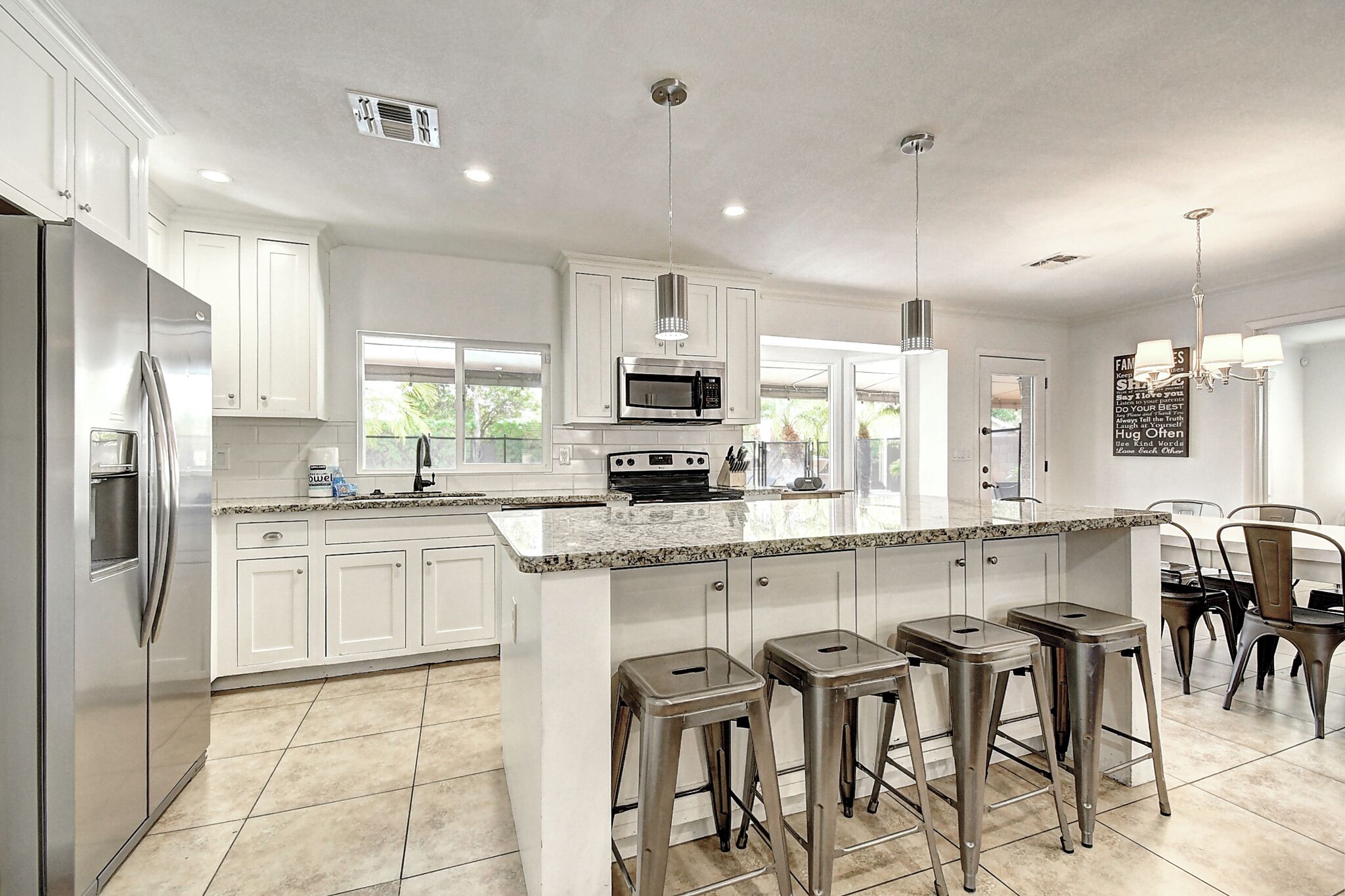 A modern kitchen with white cabinets, a stainless steel refrigerator, a microwave, and a large island with bar stools.