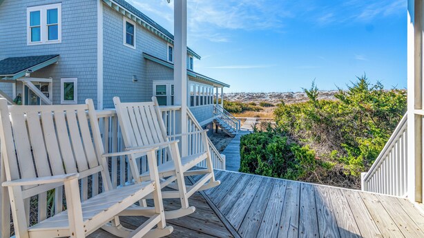 A wooden deck with rocking chairs and a view of a house with a balcony.