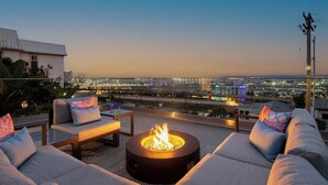 A rooftop terrace with a fire pit, outdoor seating, and a city view at dusk.