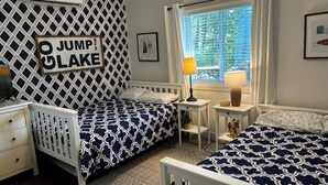 Un dormitorio con dos camas, una mesita de noche, un aparador, una ventana con persianas y un aire acondicionado de pared.