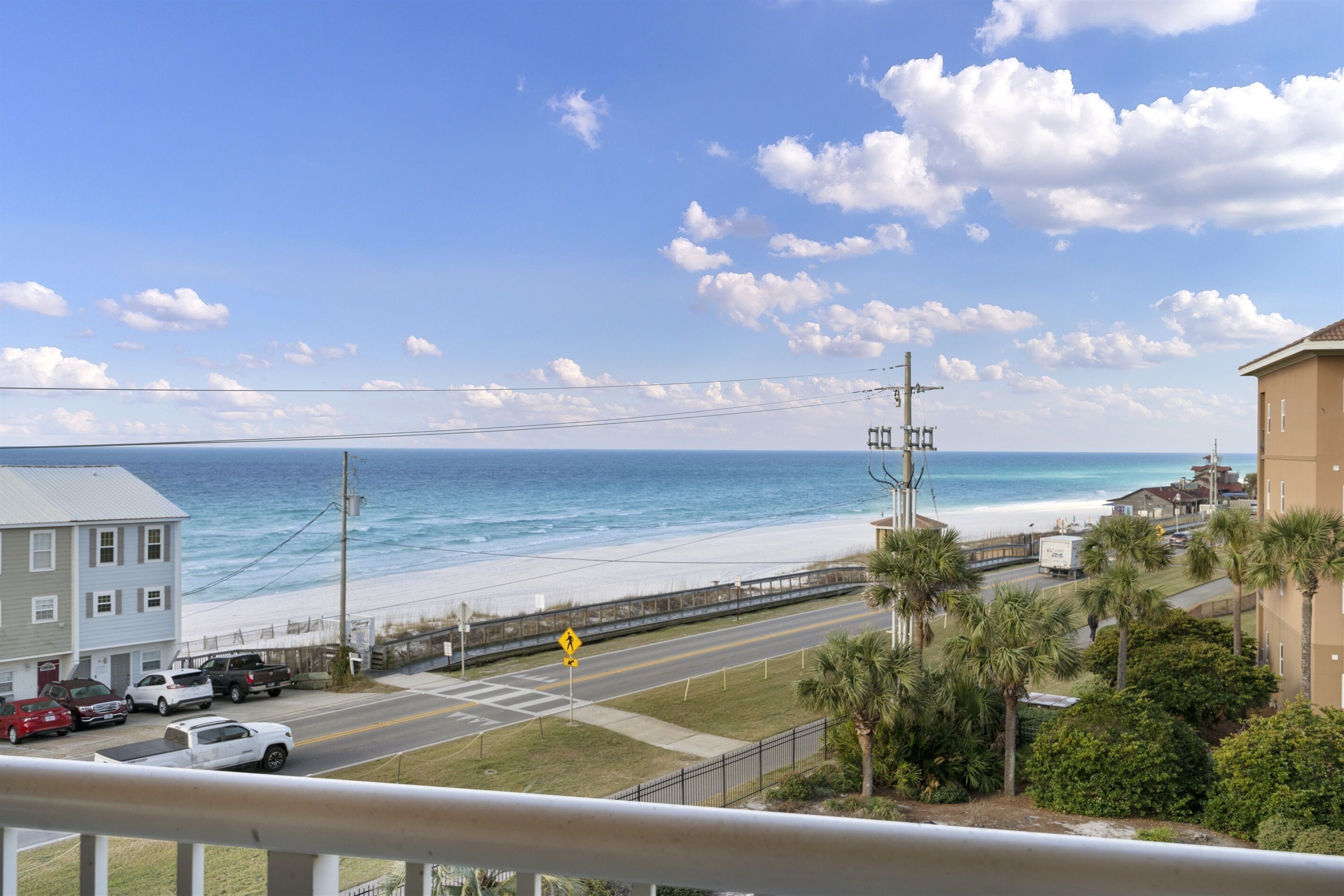 A coastal road with a beach view, a pedestrian crossing, and a building with a balcony overlooking the ocean.
