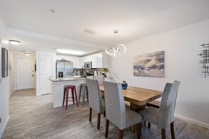 A modern kitchen with white cabinets, a wooden dining table, and grey upholstered chairs.