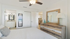 Un dormitorio con cama, tocador, ventilador de techo y espejo, con vista a la playa.